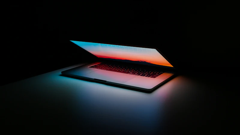 Ordinateur portable entrouvert dans le noir, écran dégradé bleu et orange